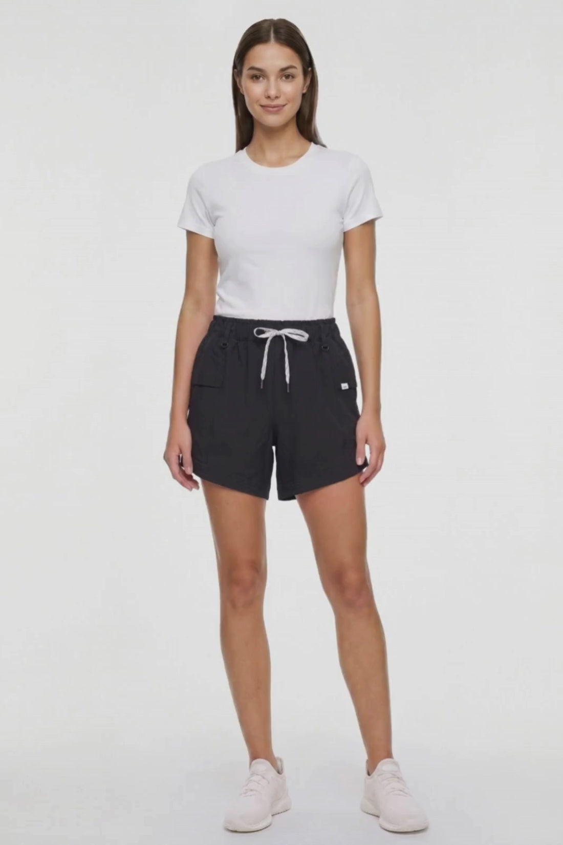 Video view of woman wearing black shorts with white drawstring waist and side pocket and white sneakers on a white background. 