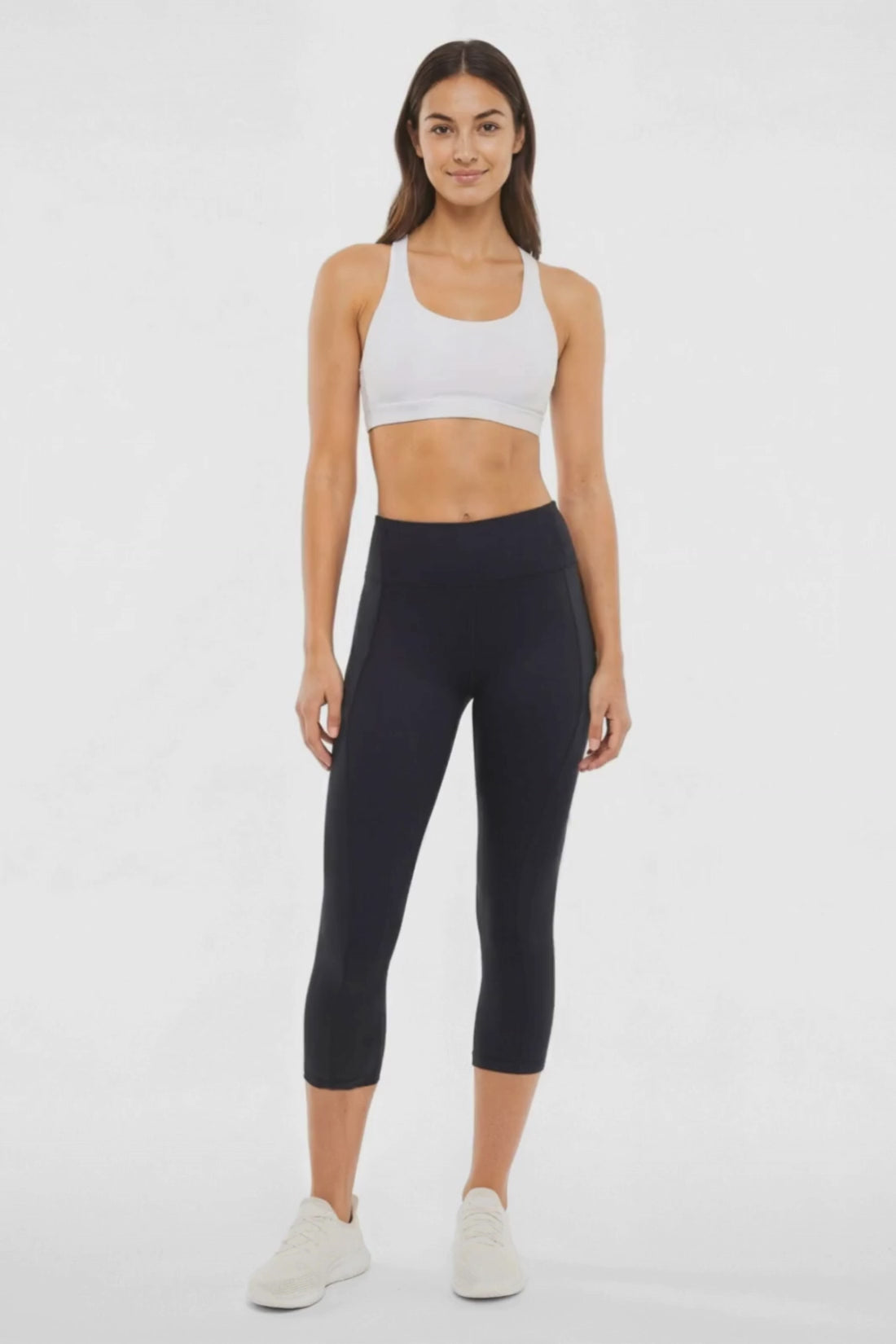 Video view of woman wearing black capris and white sneakers on a light gray background. 