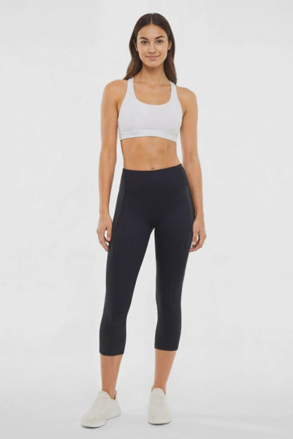 Video view of woman wearing black capris and white sneakers on a light gray background. 