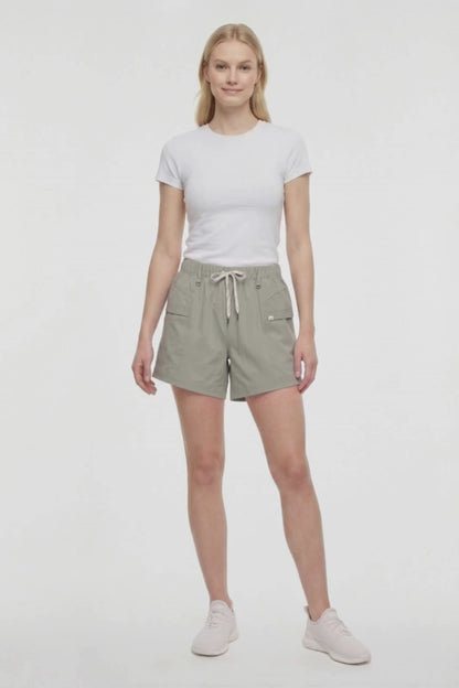Video view of woman wearing sage green shorts with white drawstring waist and white sneakers on a white background. 