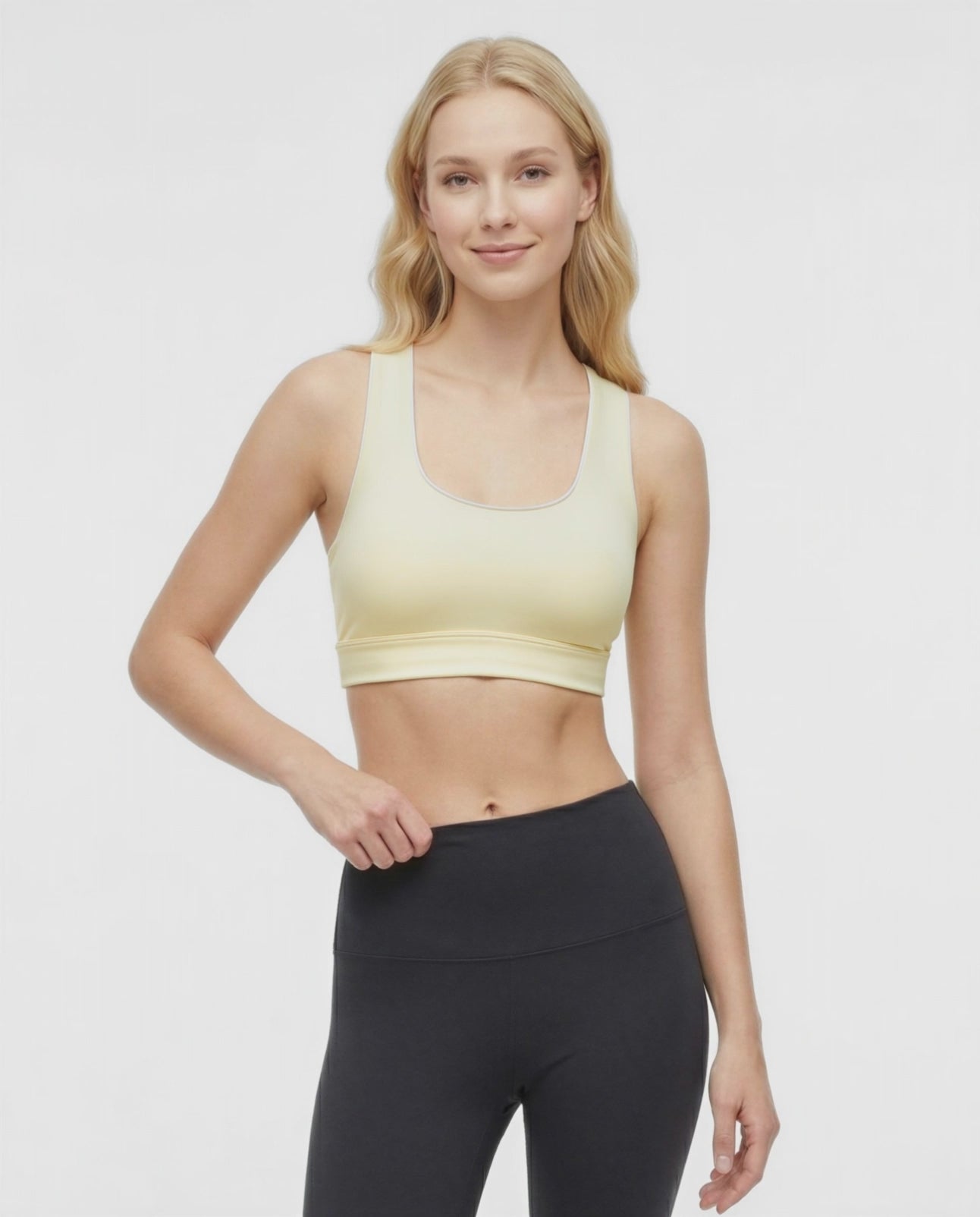 Video view of woman wearing a light yellow sports bra with white trim and black leggings on a white background. #color_french-vanilla