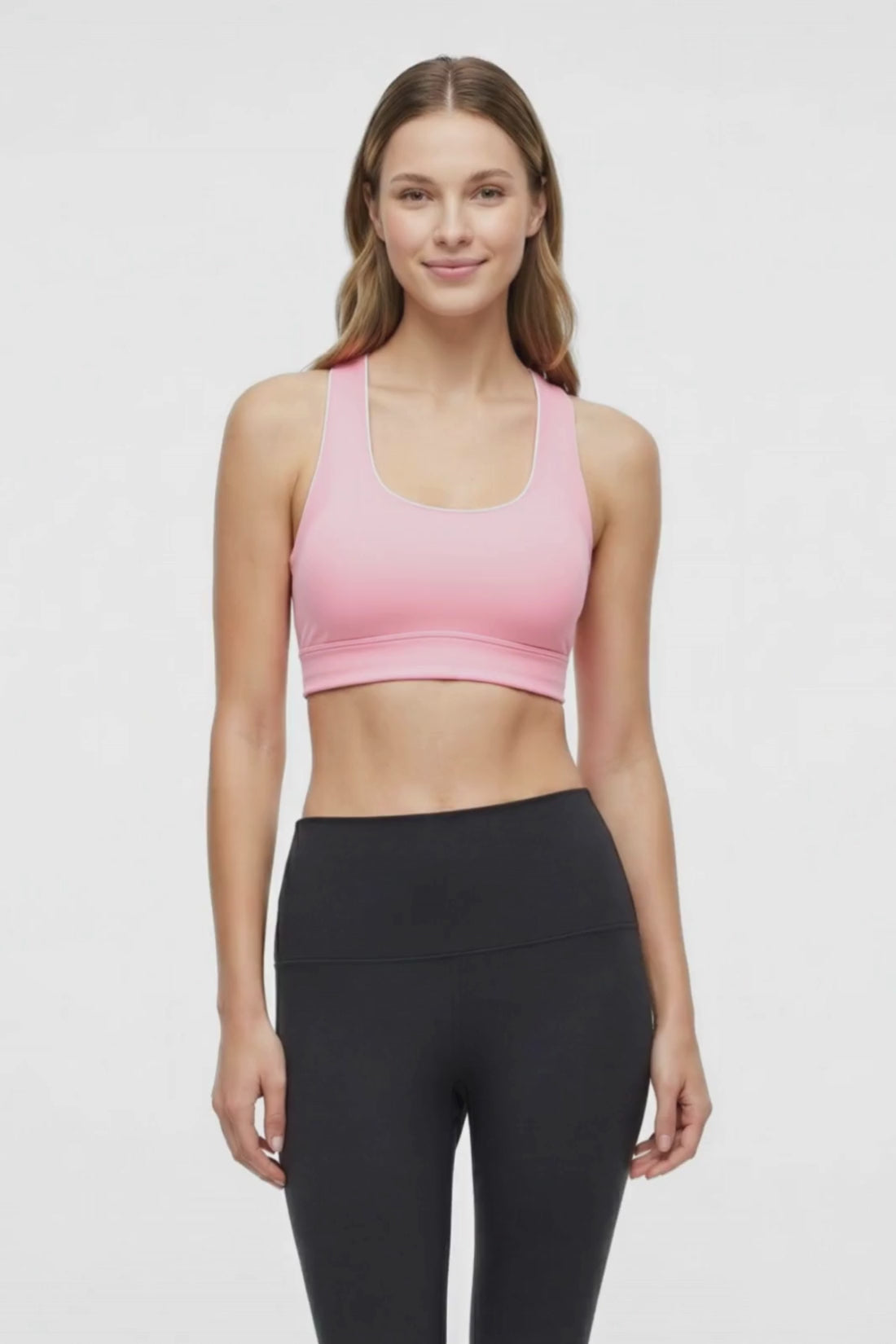 Video view of woman wearing a light pink sports bra with white trim and black leggings on a white background. 