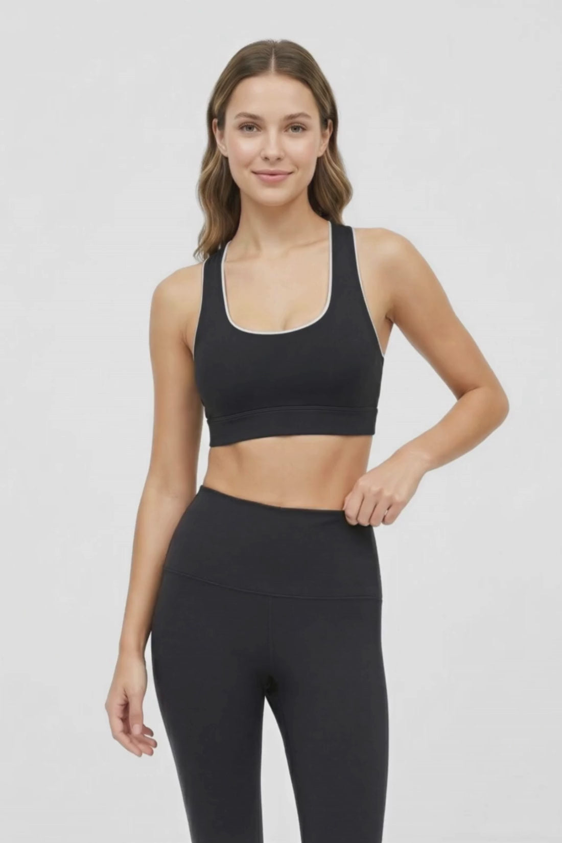 Video view of woman wearing a black sports bra with white trim and black leggings on a white background. 