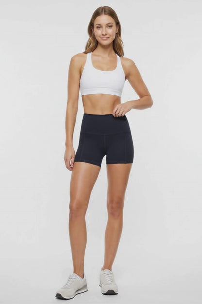 Video view of woman wearing black athletic shorts, white sports bra and white sneakers on a light background. 