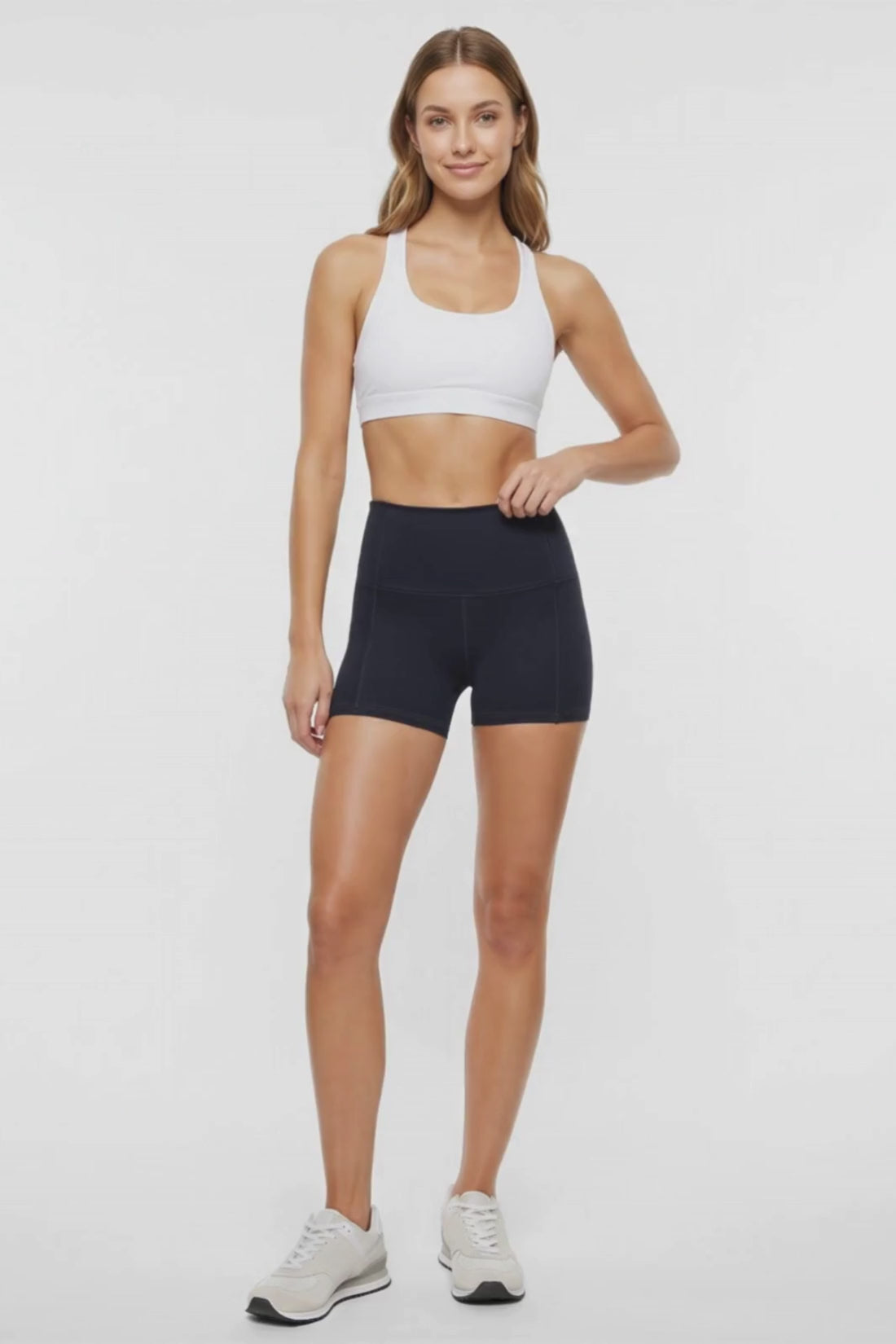 Video view of woman wearing black athletic shorts, white sports bra and white sneakers on a light background. #color_black