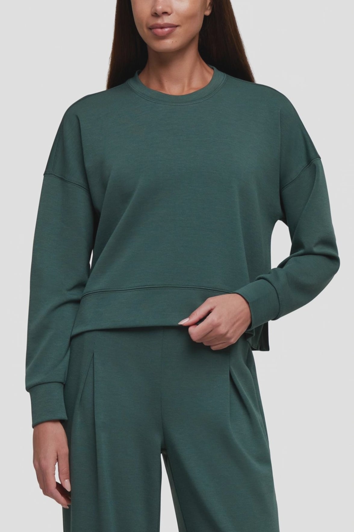 Video of a woman wearing a dark green crewneck sweatshirt and matching wide-leg sweatpants against a light gray studio background. #color_garden-topiary
