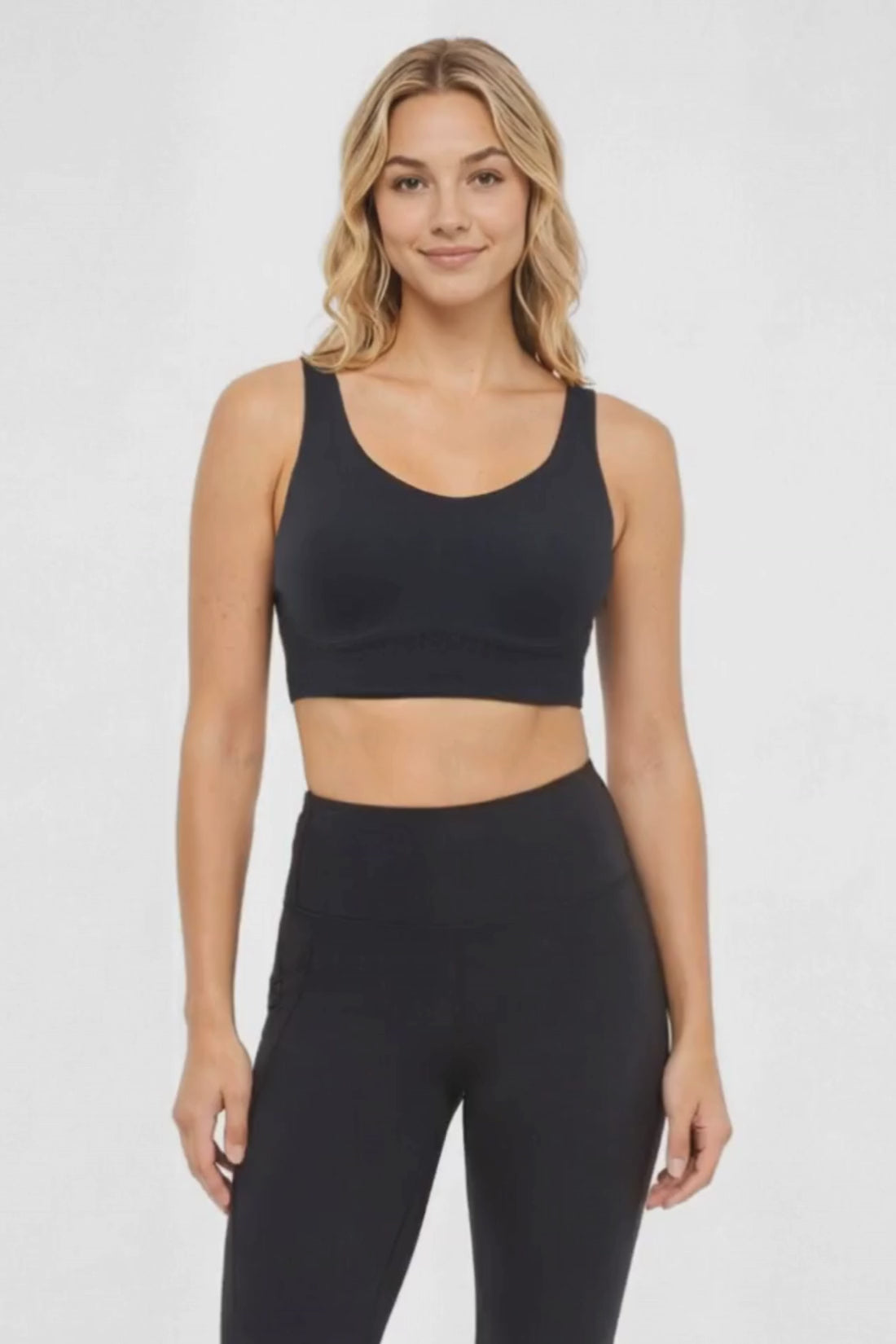 Video view of woman wearing a black sports bra and matching black leggings on a white background. #color_black