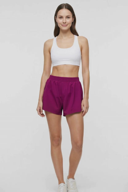 Video view of woman wearing magenta shorts and white bra on a white background. 