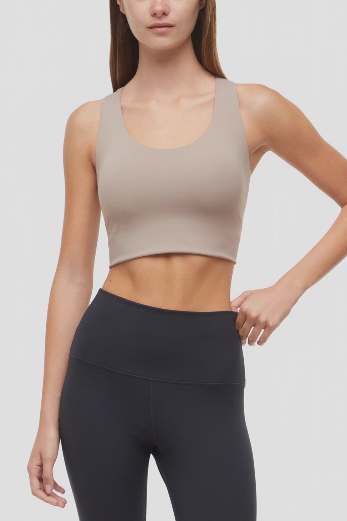 Video view of woman wearing a beige sports bra and black leggings on a white background. #color_taupe-gray