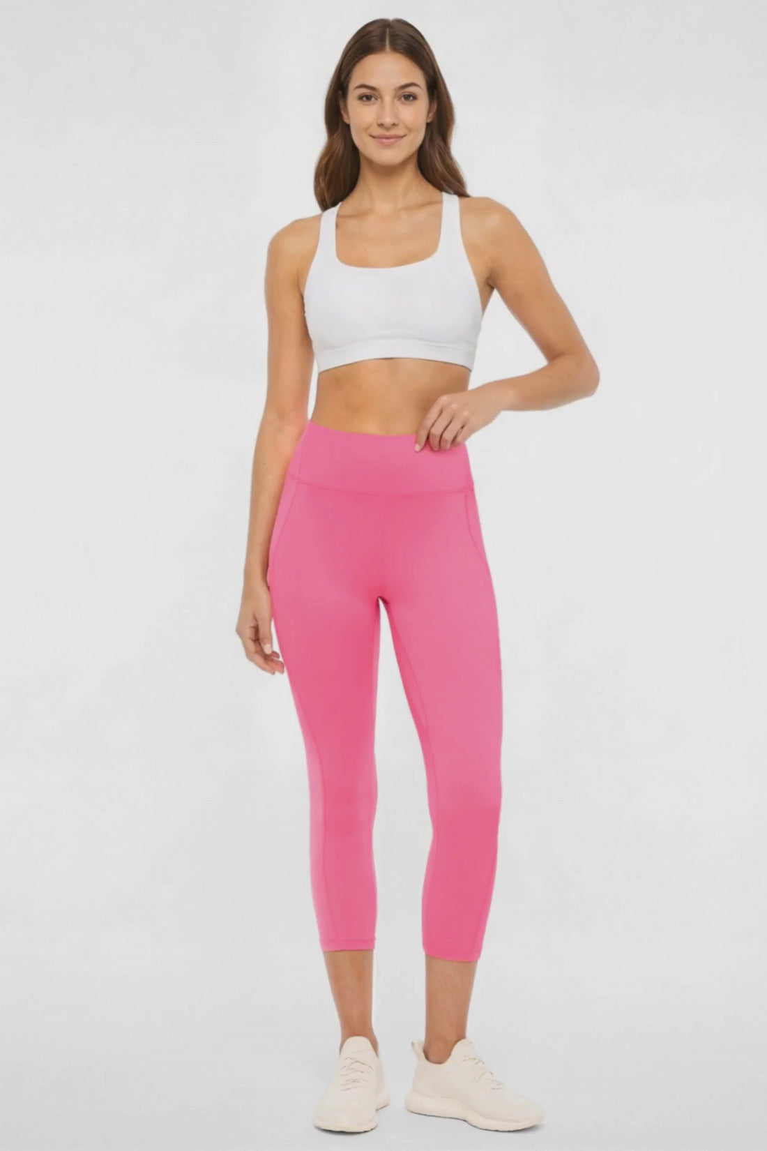 Video view of woman wearing pink capris and white sneakers on a light gray background. 
