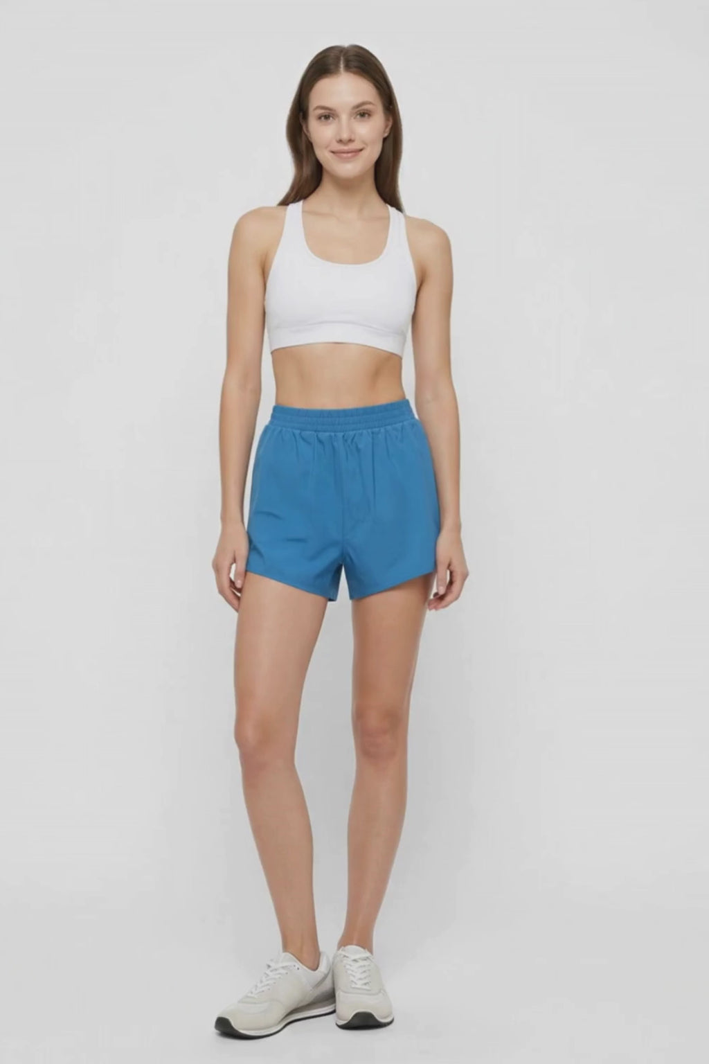 Video view of woman wearing blue shorts and white sport bra on a white background. #color_midnight
