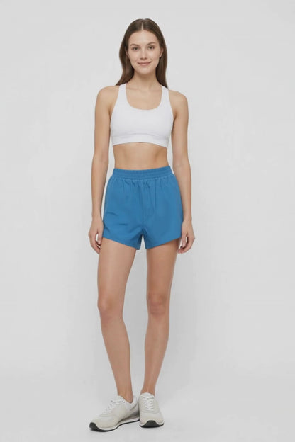 Video view of woman wearing blue shorts and white sport bra on a white background. 