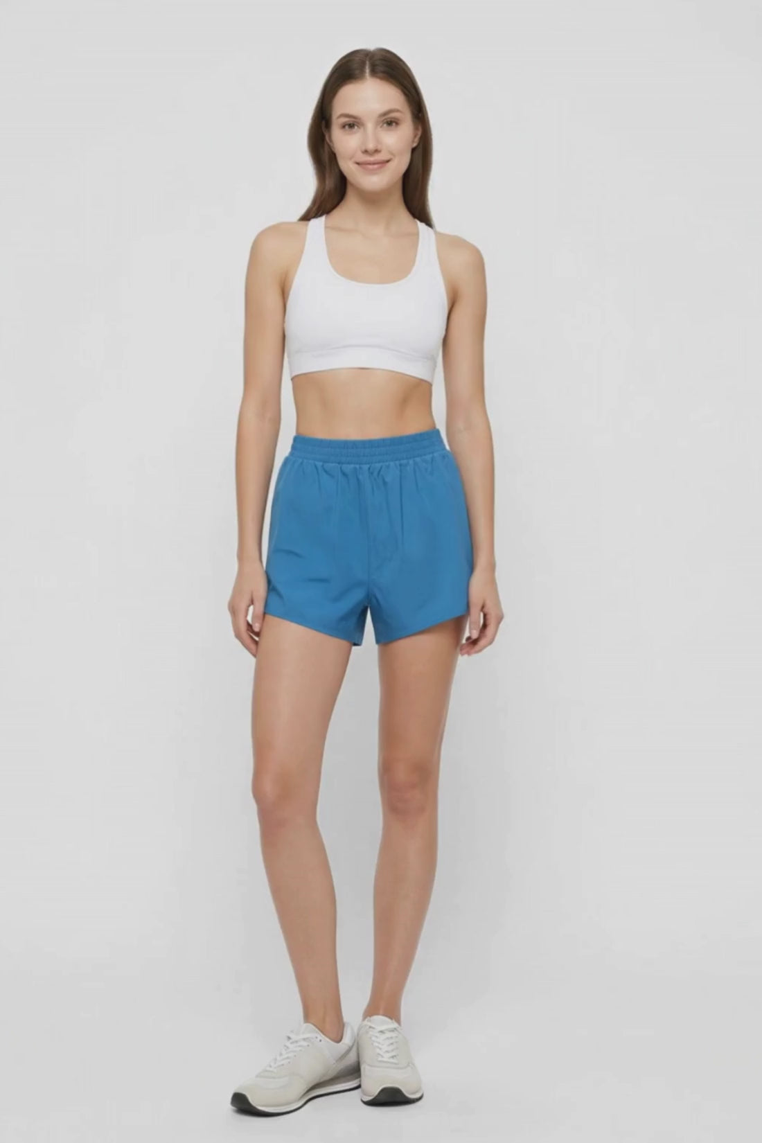Video view of woman wearing blue shorts and white sport bra on a white background. #color_midnight